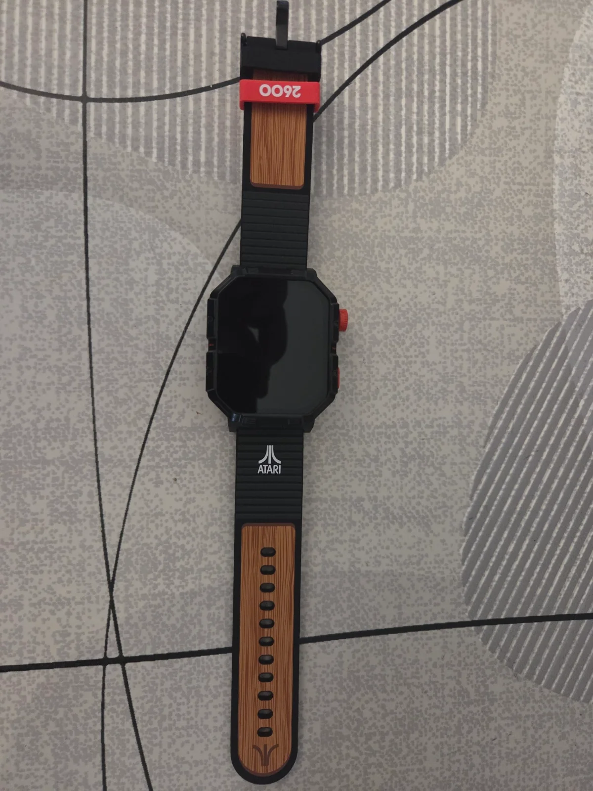 La My Play Watch Atari 2600 posée à plat, avec sa couronne rouge et son bouton dédié aux jeux